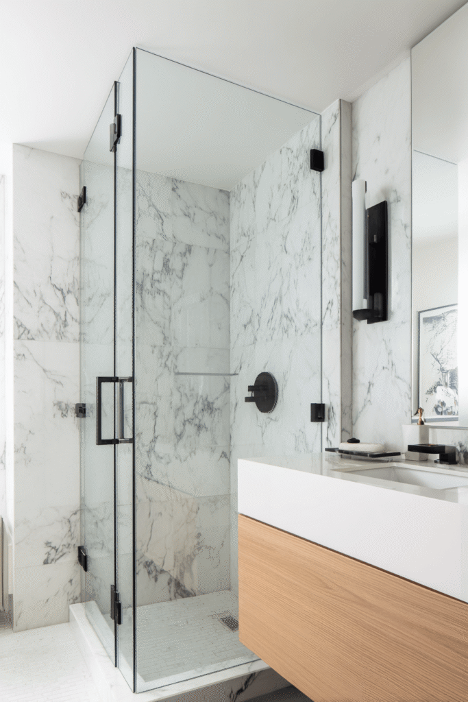 Modern New York style bathroom renovation in Toronto featuring glass walk-in shower, marble walls, and floating wood vanity.