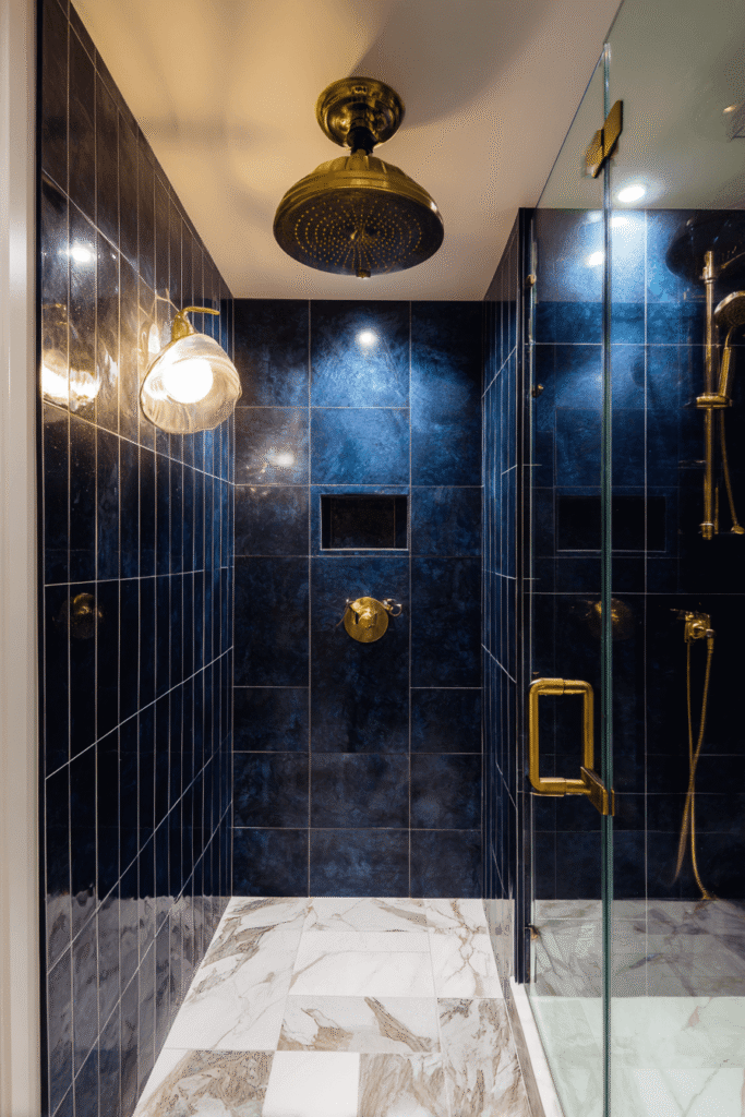 Luxury walk-in shower from a bathroom renovation Toronto project featuring navy tiles, brass rainfall showerhead, and marble flooring.