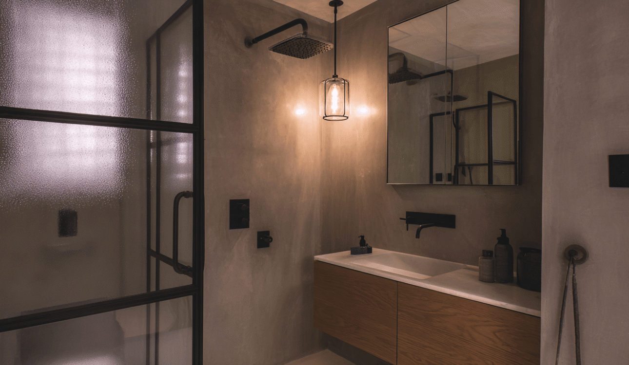 Loft-style bathroom renovation ideas in Toronto featuring a black-framed glass shower, textured walls, and modern minimalist lighting.