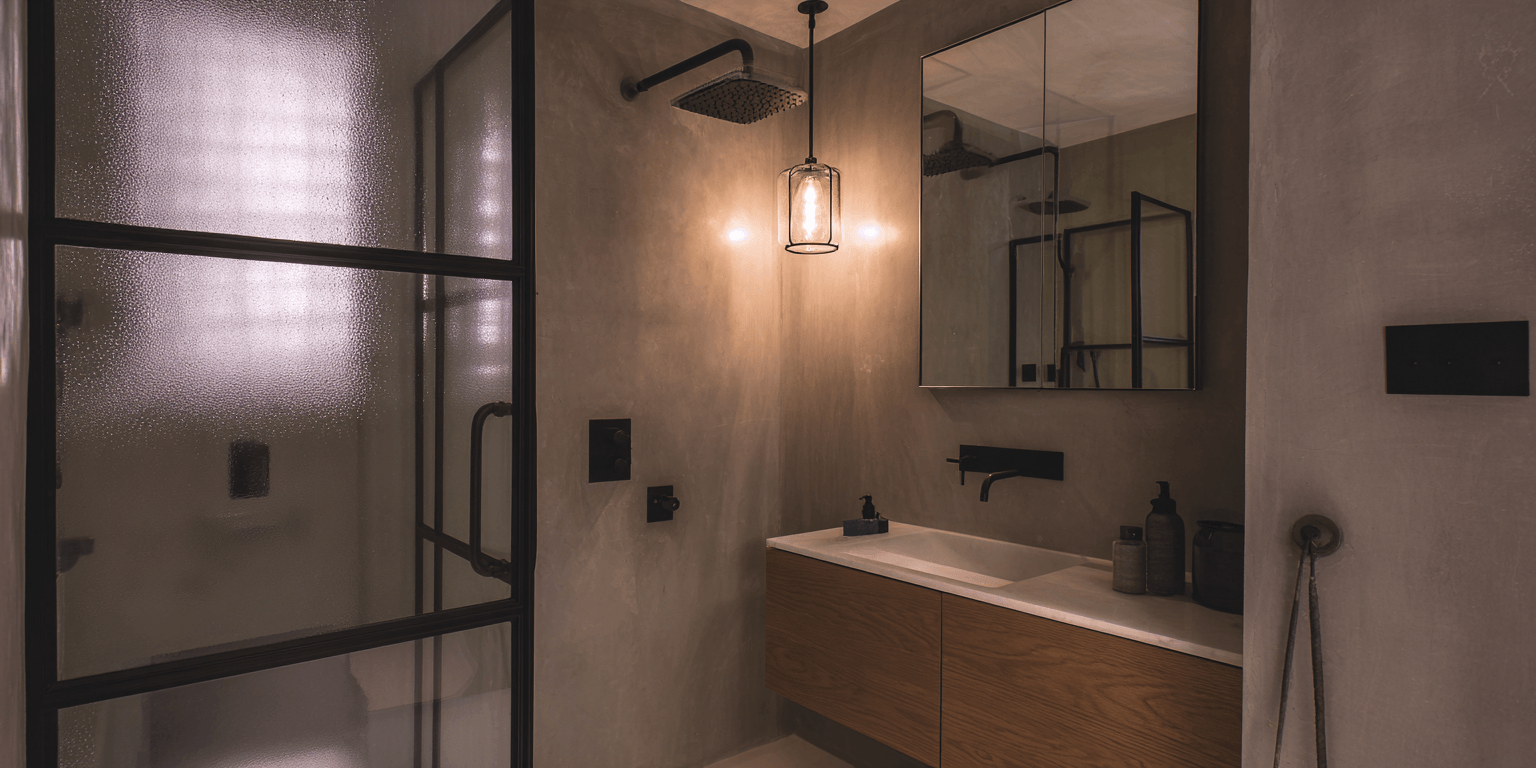 Loft-style bathroom renovation ideas in Toronto featuring a black-framed glass shower, textured walls, and modern minimalist lighting.