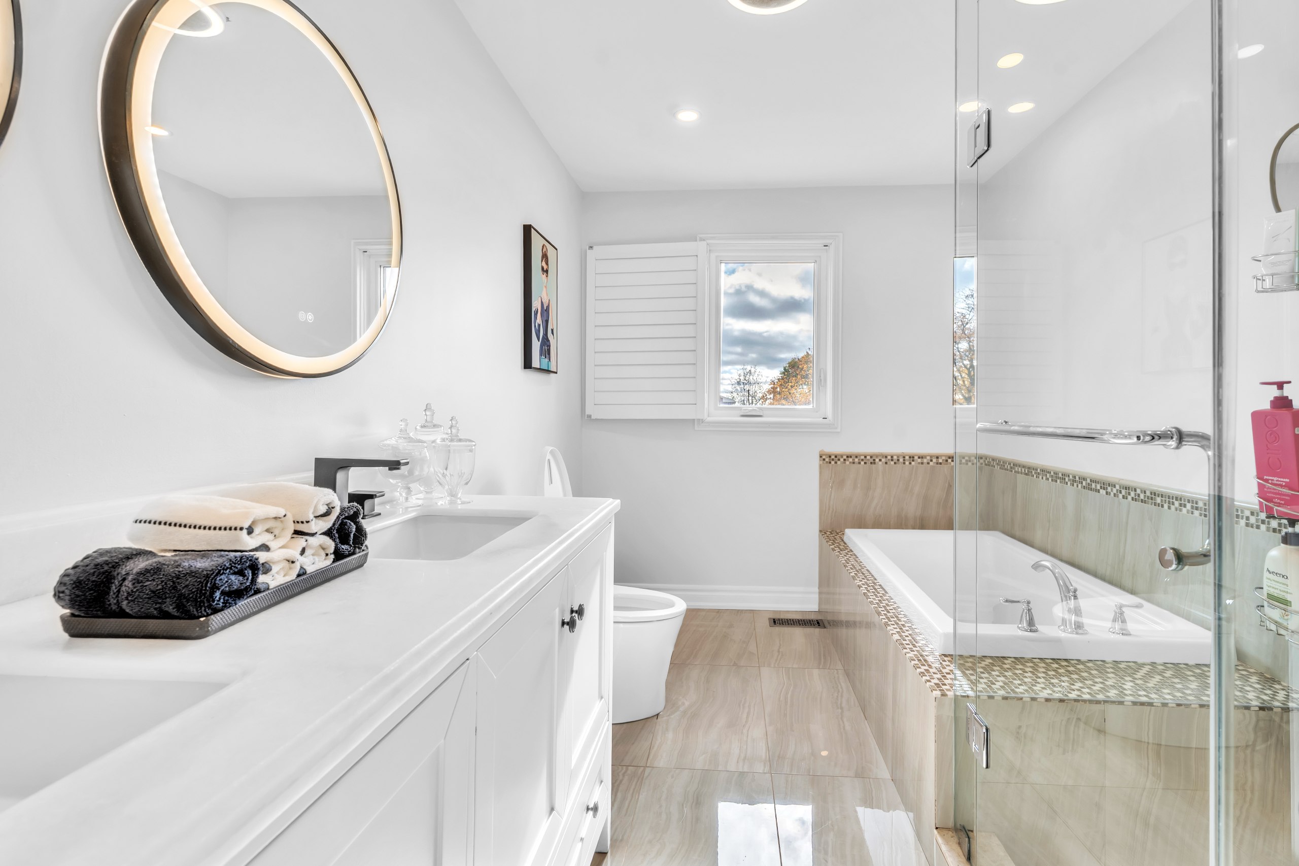 Bright bathroom renovation in Toronto with white vanity, glass shower, bathtub, and modern lighting