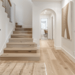 Artsy finished basement hallway with light wood stairs, white walls, natural textures, and warm decor, showing a polished approach to renovating basement entry spaces.